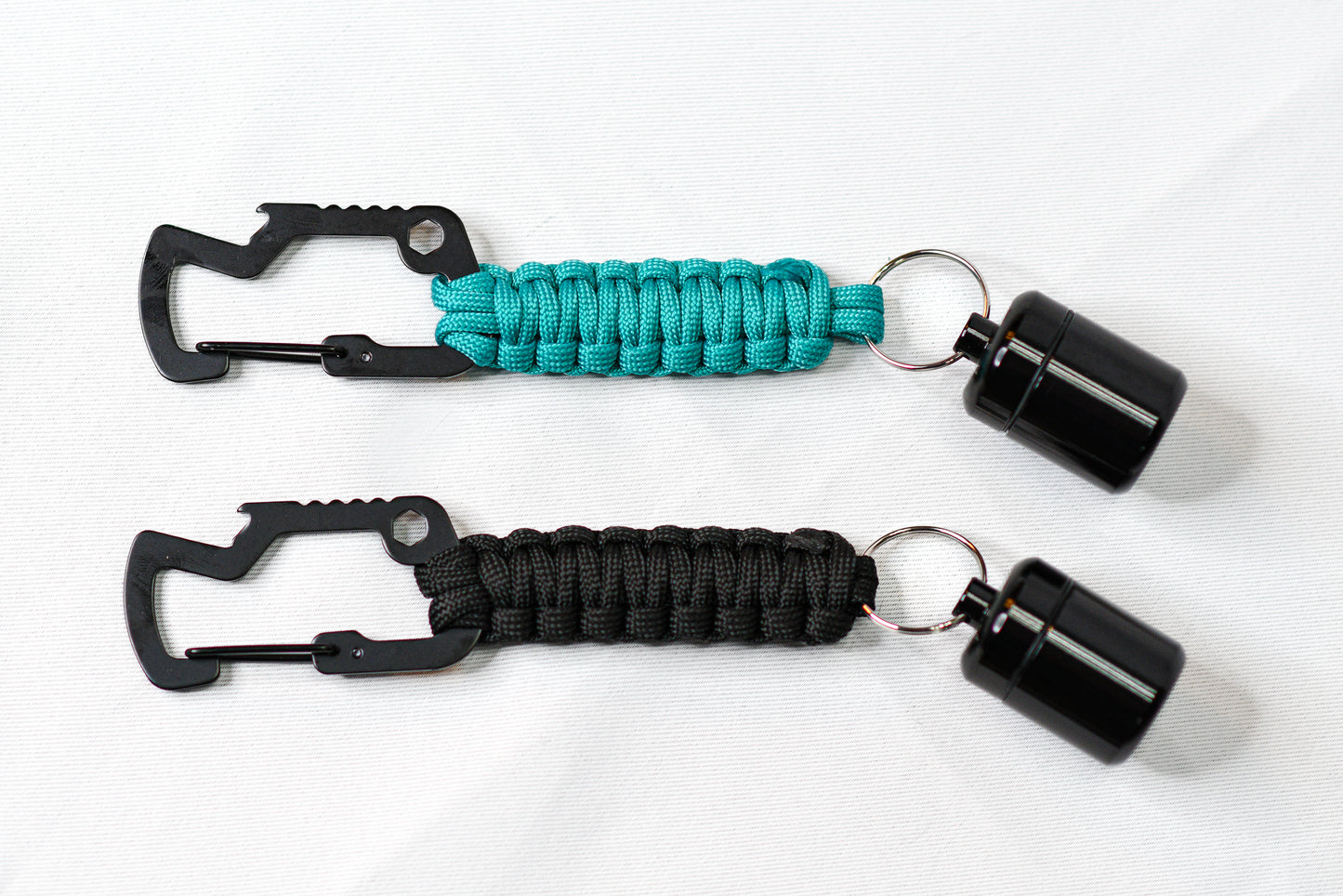 Two Ready Rolls laying next to each other, one teal and one black paracord with black carabiners and black capsules.